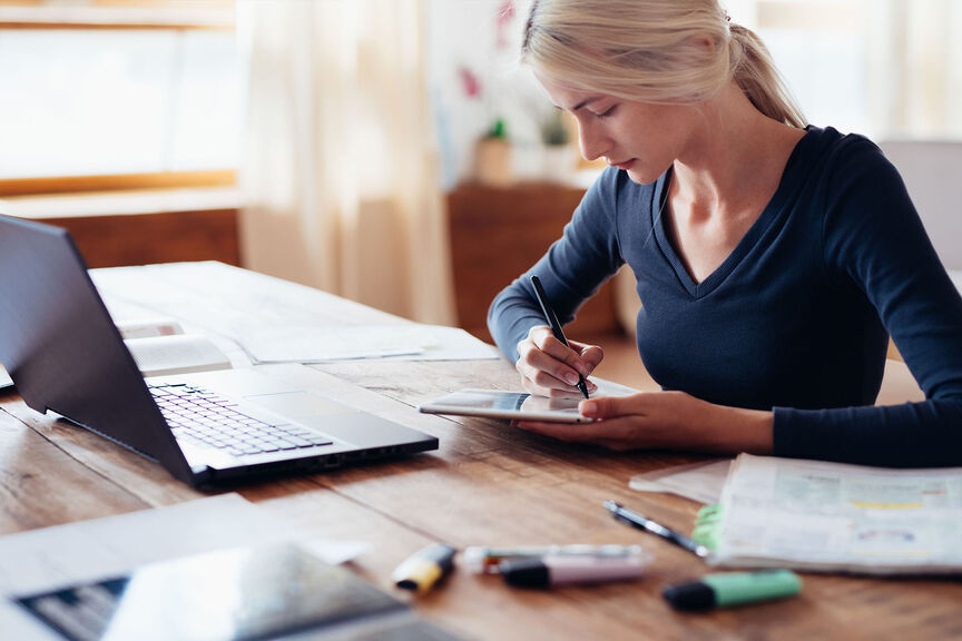 A Woman Writes on Her Tablet at Her Desk