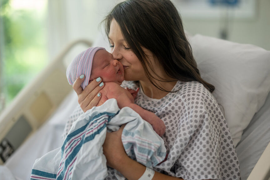 A mother kisses her newborn baby in a delivery room