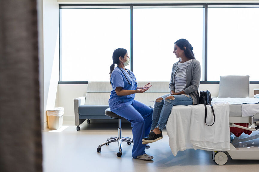 A nurse speaks with a patient in an exam room