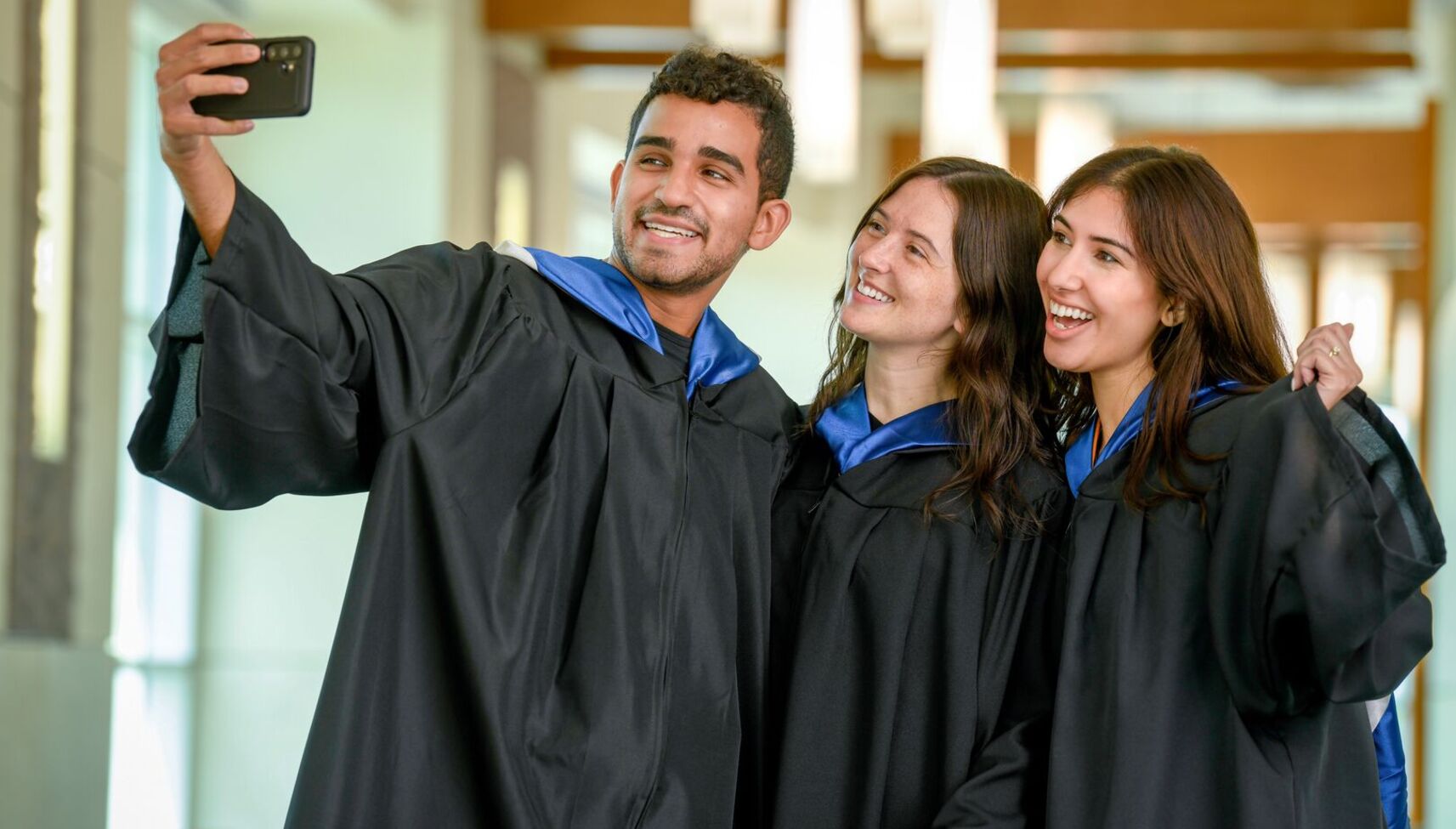 Three graduates smiling in regalia