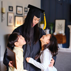A female graduate laughs and hugs her children at home